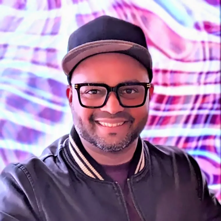 Sheldon Rodrigues smiling in front of a colourful neon wall